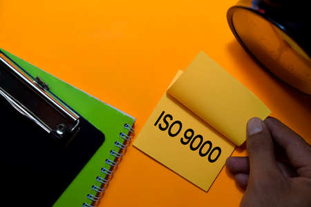 ISO 9000 write on sticky notes. Isolated on orange table backgroundの写真素材