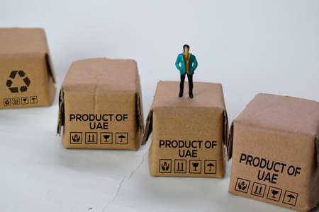 Miniature businessman Standing on Boxes with text Made in Product Of UAE isolated white bakground
