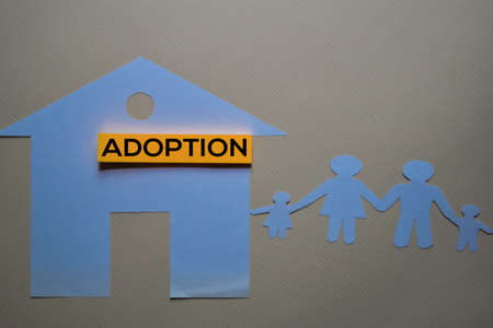 Adoption text on sticky notes with house and family made in paper on office desk.