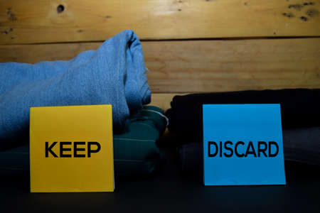 Keep and Discard write on a sticky note between fashion clothes folded and stack isolated on wooden background.の写真素材