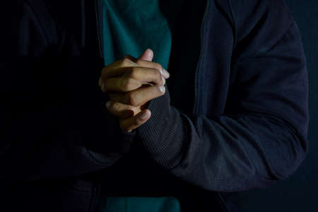 Young man worship and pray in cruch on dark black background. Christian faith or god concept....