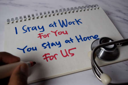 I stay at Work For You - You Stay at Home For Us write on a book and keyword isolated on Office Desk. Healthcare/Medical Conceptの写真素材