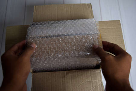 A young man holding bubble warp and box inside for protection delivery.