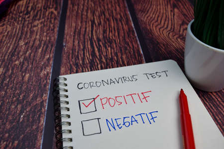 Coronavirus and check positive disease write on a book Isolated on wooden table backgroundの写真素材