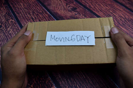 Moving Day write on a sticky note above brown box Isolated on wooden table backgroundの写真素材