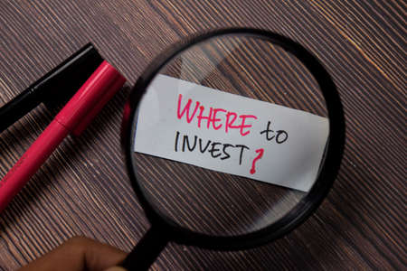 Where To Invest? write on sticky note with Magnifying Glass isolated on wooden table.の写真素材