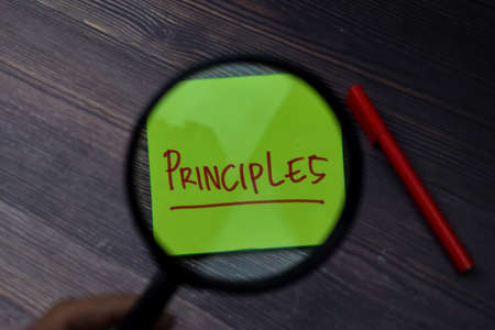 Principles write on sticky note with magnifying glass isolated on wooden table.の写真素材