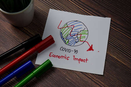 Covid 19 - Economic Impact write on sticky note isolated on wooden table.の写真素材