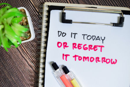 Concept of Do It Today or Regret it Tomorrow write on paperwork isolated on Wooden Table.の写真素材