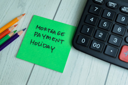 Concept of Mortgage Payment Holiday write on sticky notes with calculator isolated on Wooden Table.の写真素材