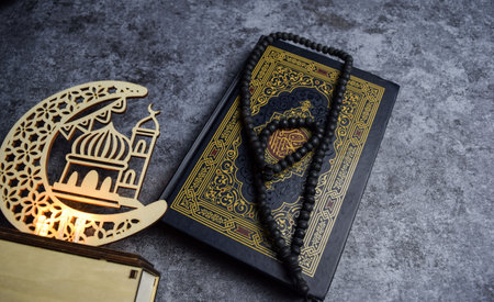 The holy quran, prayer beads, golden ramadhan lamp with islamic rosary beads on dark background...
