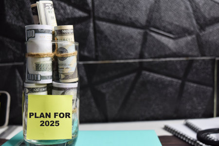 Concept of Plan for 2025 write on sticky notes with dollars in glass jar