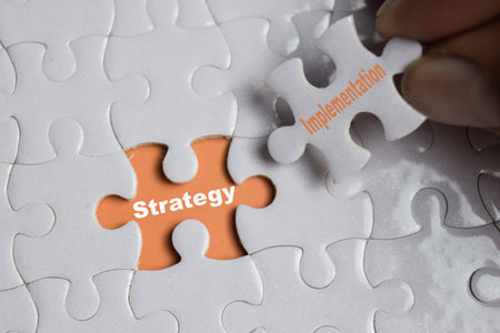 Hand holding piece of jigsaw puzzle with word Strategy Implementation. Business and finance conceptの写真素材