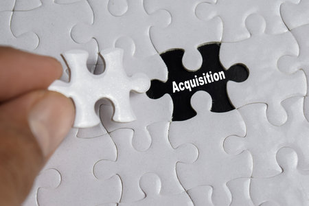 Hand holding piece of jigsaw puzzle with word Acquisition. Business and finance conceptの写真素材