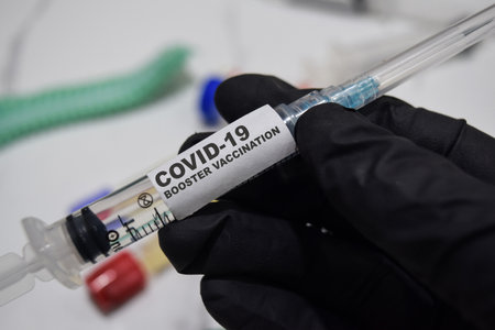 Covid-19 booster vaccination drug syringe in black gloved hands. Medical conceptの写真素材