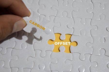 Hand holding piece of jigsaw puzzle with word carbon and offset.の写真素材