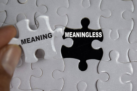 Hand holding piece of jigsaw puzzle with word meaning and meaningless. Business and finance conceptの写真素材