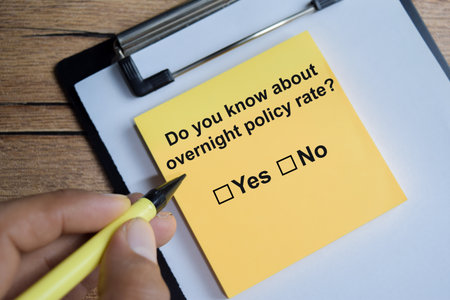 Do you know about overnight policy rate write on sticky notes isolated on Wooden Table. A person is...