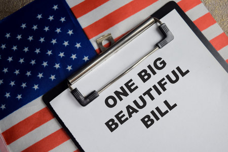 Concept of one big beautiful bill with the United States flag write on clipboard isolated on Wooden Table.の写真素材