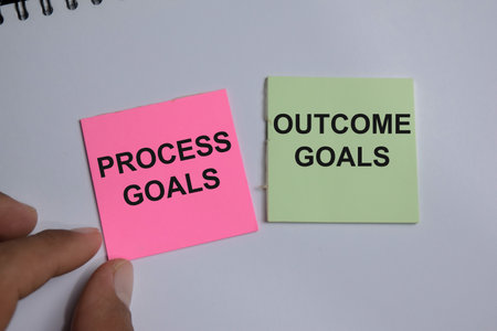 Concept of process goals and outcome goals write on sticky notes isolated on Wooden Table.