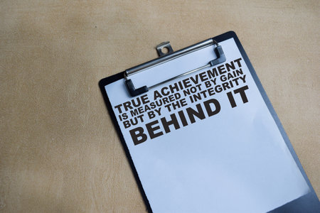 Concept of true achievement is measured not by gain but by the integrity behind it write on clipboard isolated on Wooden Table.の写真素材