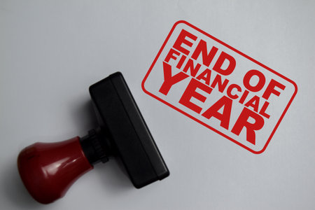 Red Handle Rubber Stamper and end of financial year text above book isolated on wooden background