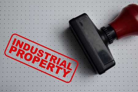 Red Handle Rubber Stamper and industrial property text above book isolated on wooden background. For factory ownership, legal rights and business protectionの写真素材