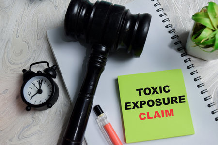 Concept of toxic exposure claim write on sticky notes isolated on Wooden Table. Representing legal...