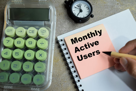 Concept of monthly active users write on sticky notes isolated on Wooden Table. Ideal for marketing...