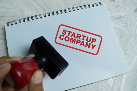 Red Handle Rubber Stamper and startup company text above book isolated on wooden background. For new corporate entities and venture capital investment