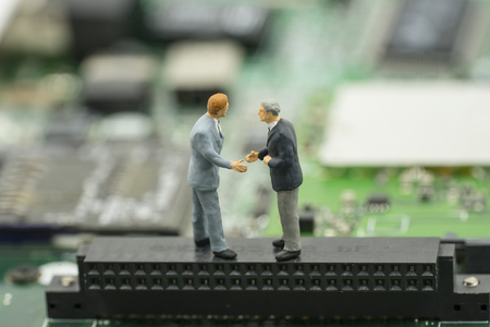 business agreement by two mini businessman shake hand on mainboard background - can use to display...
