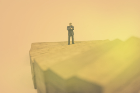 abstract mini businessman stand on wood block step with vintage filter - can use to display or montage on productの写真素材