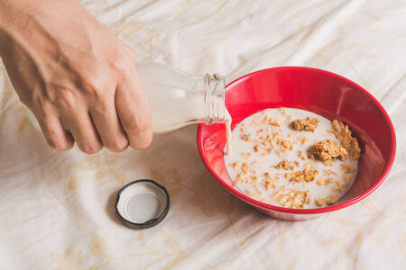 Hand pour milk into Cereals in red bowlの写真素材