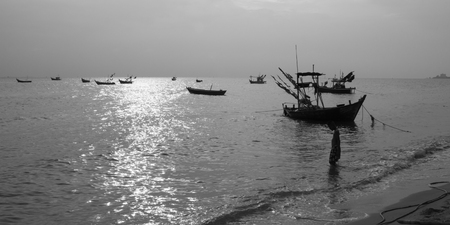 black and white tone child walk in to sea near fishing boat at bangsean chonburi thailandの写真素材