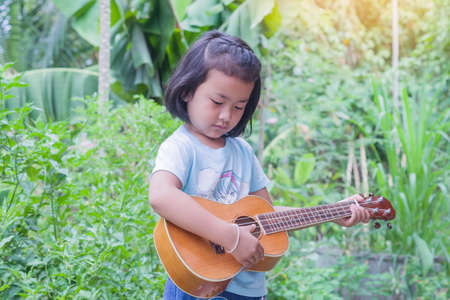Asian little girl stand playing  ukulele on natural background.の写真素材