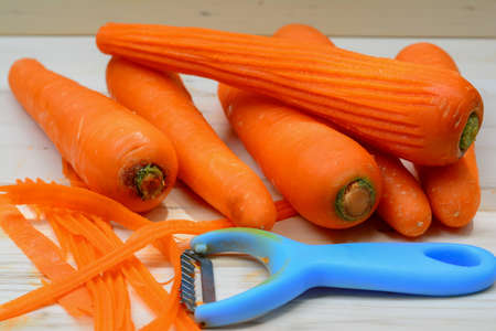 Raw carrots and peeler on wooden tableの写真素材