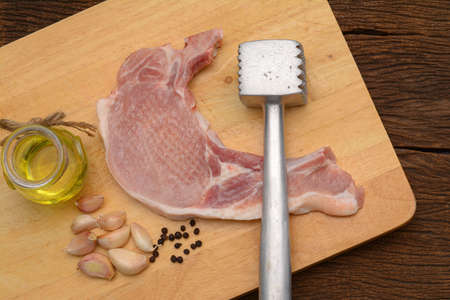 Raw steak with meat hammer and ingredient on wooden board