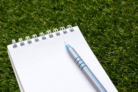 Notepad with blue pen on artificial green grassの写真素材