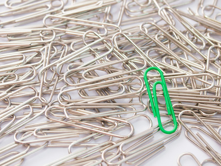 Green paper clip stand different from the crowd on white backgroundの写真素材