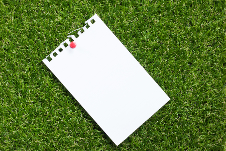 Blank note placed on artificial green grass backgroundの写真素材