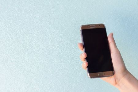 Bangkok, Thailand September 10, 2016 : Woman held android phone Samsung galaxy S7 Edge on blue concrete background. Samsung S7 Edge is smart phone with multi touch screenのeditorial素材