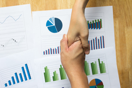 Man and female shake hand over financial, business graph and chartの写真素材