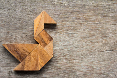 Wooden tangram as bird shape on old wood backgroundの写真素材