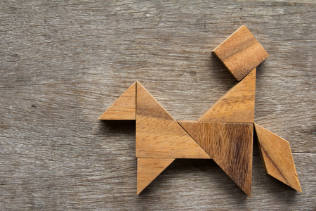 Wooden tangram as man ride the horse shape on old wood backgroundの写真素材