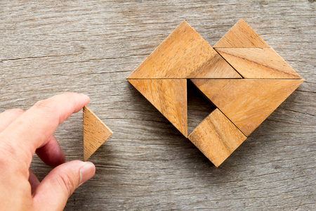 Man held piece of tangram puzzle to fulfill the heart shape on wooden table (Concept of love)の写真素材