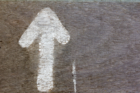 Grunge white paint arrow on brown wood background