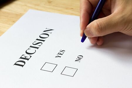 Decision paper with yes and no choice with man hold the pen on wood backgroundの写真素材