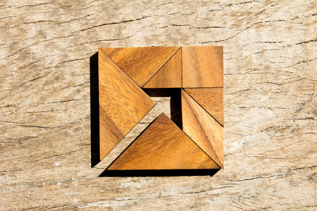 Tangram puzzle as arrow in square shape on wooden background (Concept for business direction and decision)の写真素材