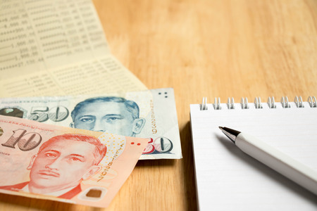 Bank passbook with Singapore dollar and book with pen on wood table background