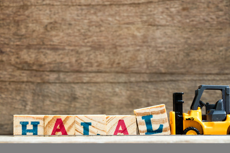 Yellow plastic toy forklift hold letter block L to complete word halal on wood background